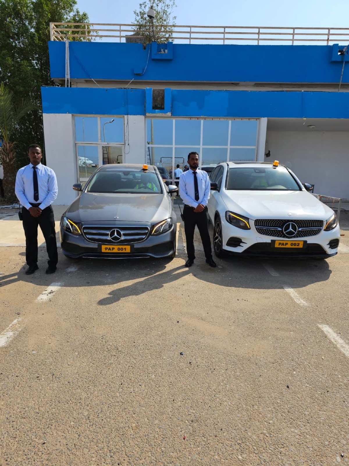 Two uniformed SAS chauffeurs flanking a grey Mercedes E-Class and white GLC on the apron